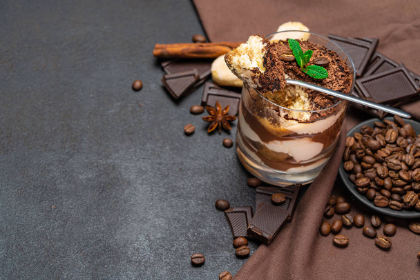 Classic tiramisu dessert in a glass cup and pieces of chocolate on dark concrete background - Foto, Bild