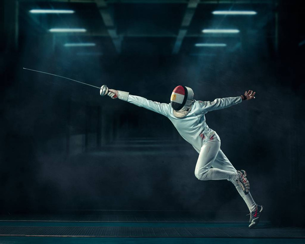 Shallow focus shot of a person fencing  with a fencing mask and an epee in a dark room - Valokuva, kuva
