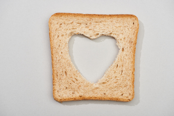 Top view of bread slice with carved heart shape on grey background - Φωτογραφία, εικόνα