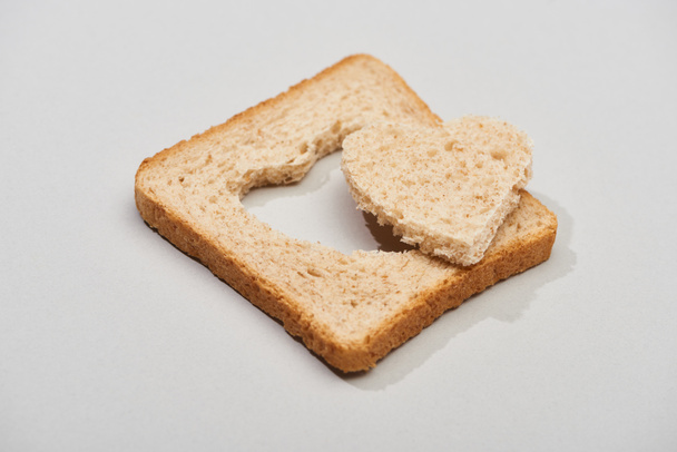 Slice of bread with carved heart shape on grey background - Foto, Imagem