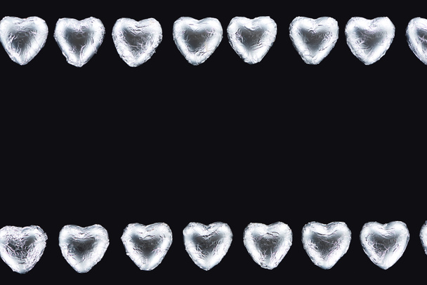 Top view of lines from heart shaped sweets in foil isolated on black - Foto, imagen