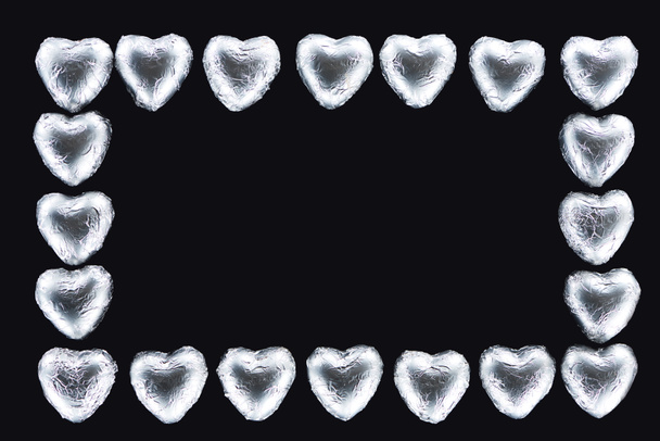 Vista superior del marco de caramelos en forma de corazón en lámina aislada en negro
 - Foto, imagen