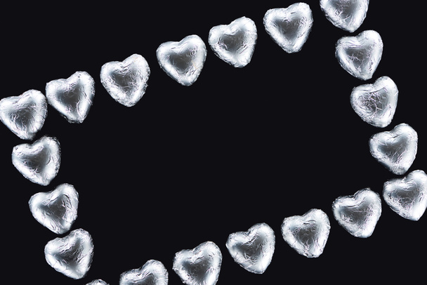 Вид сверху рамы с конфетами в форме сердца в фольге, изолированной черным цветом с пространством для копирования
 - Фото, изображение