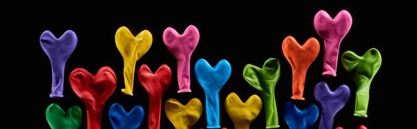 Top view of colorful rubber balloons in heart shape isolated on black, panoramic shot  - Foto, imagen