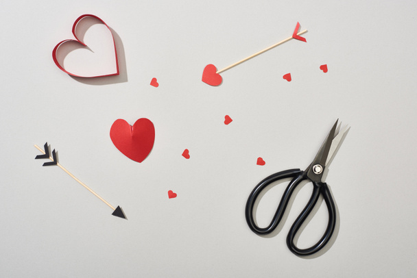 Top view of heart shaped papers with arrows and scissors on grey background - Photo, Image