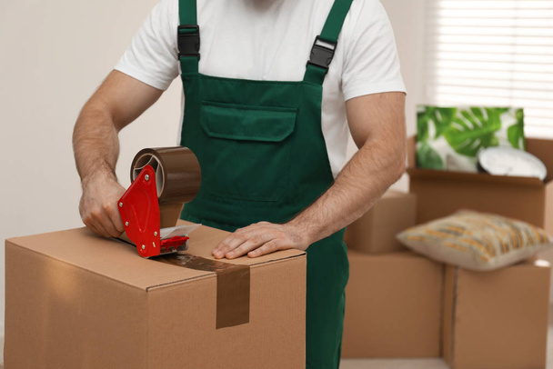 Man packing box with adhesive tape indoors, closeup. Moving serv - Fotó, kép