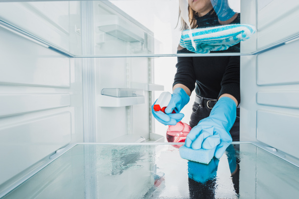 Vista ritagliata della donna in guanti di gomma pulizia frigorifero con detergente isolato su bianco
 - Foto, immagini