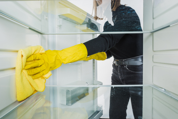 Vágott kilátás nő gumikesztyűben takarítás hűtőszekrény ronggyal elszigetelt fehér - Fotó, kép