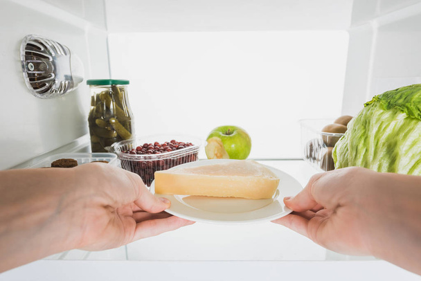 白で隔離された果物や漬物で冷蔵庫からチーズを取る女性の作物ビュー - 写真・画像
