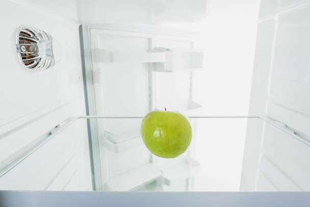 Sappige groene appel in koelkast met open deur geïsoleerd op wit - Foto, afbeelding