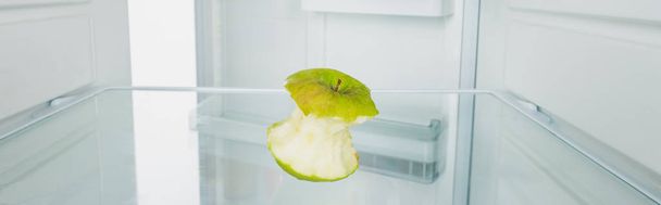 Panoramic shot of gnawed green apple in refrigerator with open door isolated on white - Photo, Image