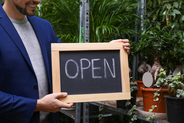 Male business owner holding OPEN sign in his flower shop, closeu - Foto, afbeelding