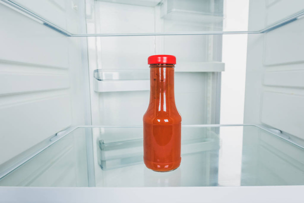 Bottle of tomato sauce in fridge with open door isolated on white - Fotó, kép