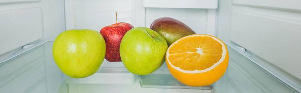 Panoramic shot of fresh mango with apples and orange slice on refrigerator shelf  - Фото, зображення