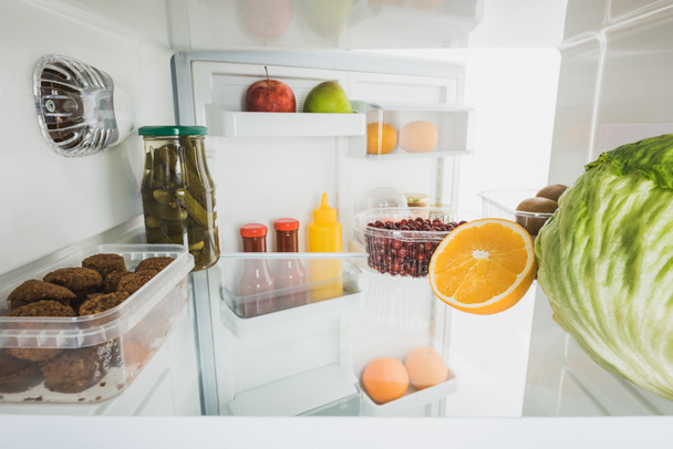 Cutlets met rijp fruit en kool in koelkast met open deur geïsoleerd op wit - Foto, afbeelding