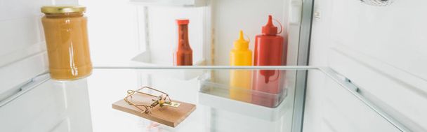 Panoramic shot of mousetrap in fridge with sauces and open door isolated on white - Photo, Image