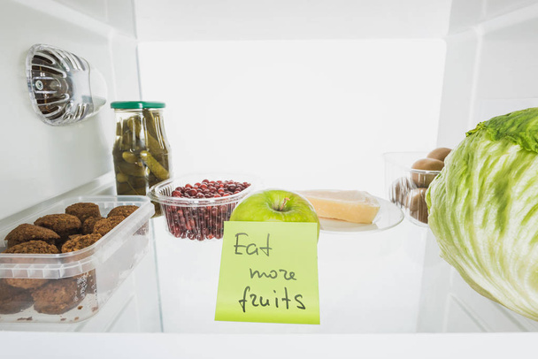 Tarjeta con comer más letras de frutas en la nevera estante con alimentos aislados en blanco
 - Foto, Imagen