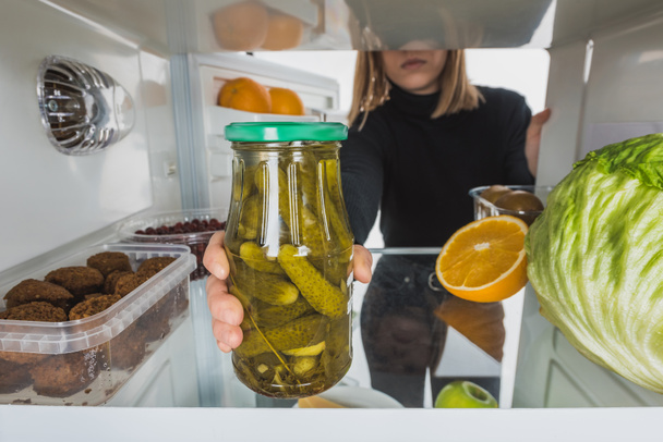 Cropped view of woman taking far with pickles from fridge shelf isolated on white - Photo, Image