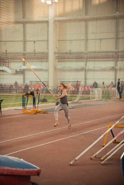 Skok na tyči na sportovním stadionu - mladá sportovkyně s culíkem v rukou - Fotografie, Obrázek