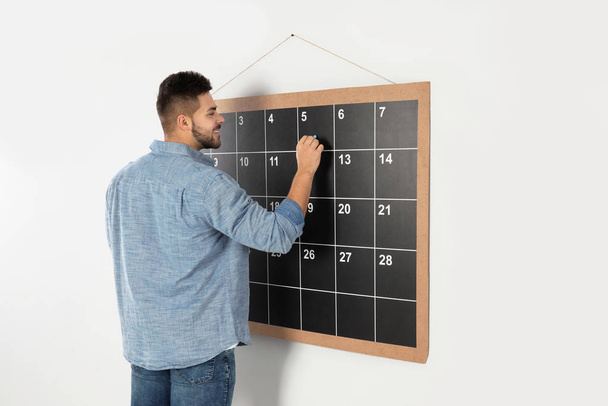 Young man writing with chalk on board calendar - Foto, Imagem