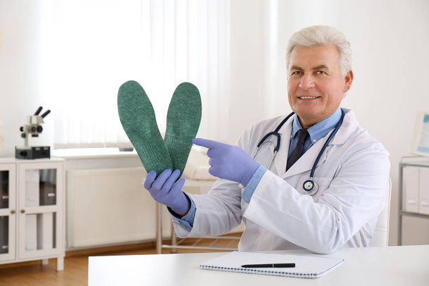 Senior male orthopedist showing insoles in clinic - Photo, Image