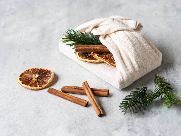 Milieuvriendelijke stof herbruikbare geschenkverpakking met sparren brunch, kaneelstokje en droog oranje plakje. Kerstmis herbruikbare duurzame cadeauverpakking alternatief. - Foto, afbeelding
