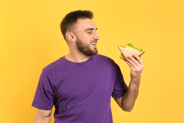 Young man eating tasty sandwich on yellow background - Zdjęcie, obraz