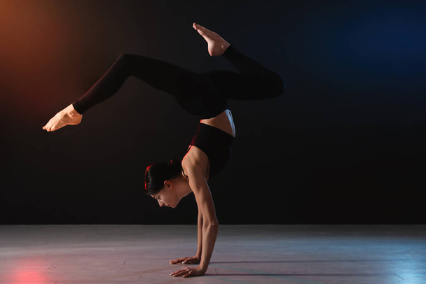 Young professional acrobat exercising in dark studio - Фото, зображення