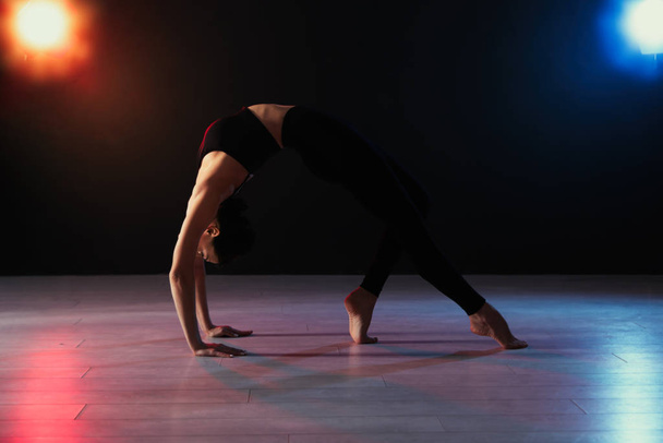 Young professional acrobat exercising in dark studio - 写真・画像