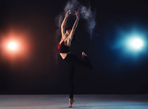 Professional acrobat with chalk powder exercising in dark studio - Foto, Imagem