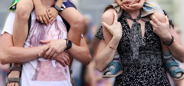 Padres sosteniendo a sus hijos sobre los hombros durante la actuación en la calle, fondo borroso
  - Foto, Imagen