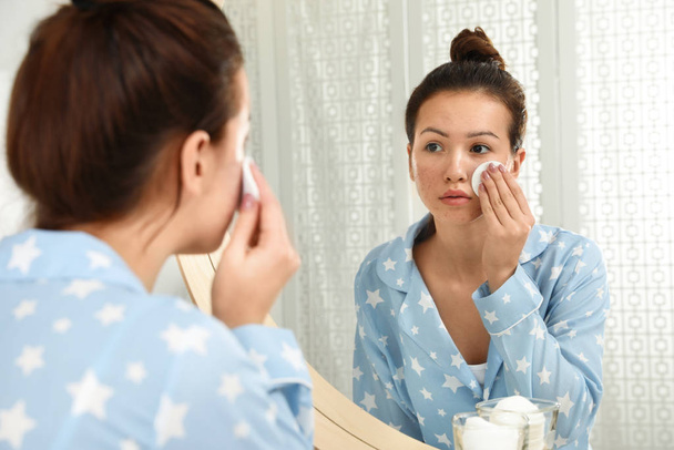 Дівчина-підліток з проблемами акне прибирання її обличчя біля дзеркала в кажані
 - Фото, зображення