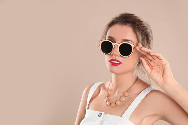 Young woman wearing stylish sunglasses on beige background. Spac - Foto, imagen
