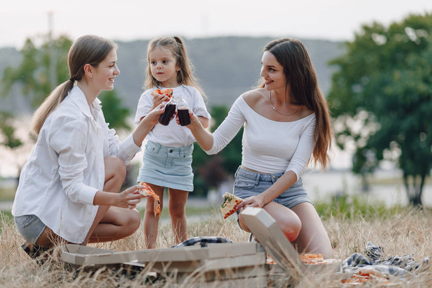 klein meisje hebben plezier bij picknick, pizza, drankjes, zomer en gazon - Foto, afbeelding