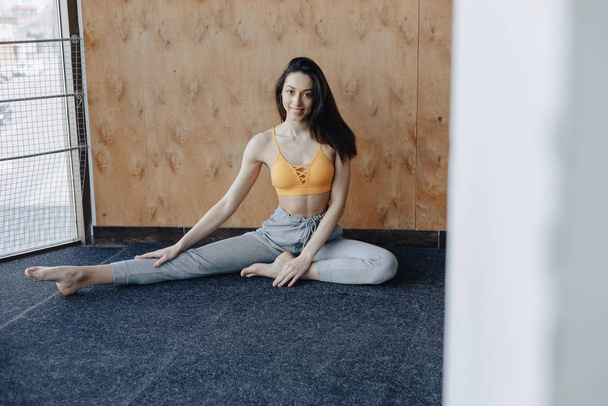 Giovane ragazza attraente che fa esercizi di fitness con yoga sul pavimento su uno sfondo di legno
 - Foto, immagini