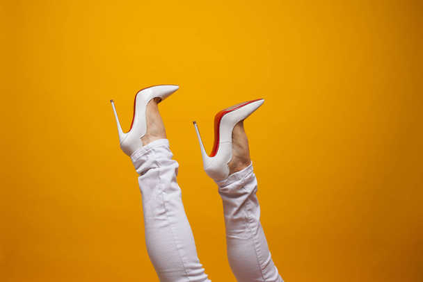 Female feet in beautiful white stiletto shoes, yellow background copy space. - Fotó, kép