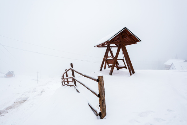 fa kerítés és swing havas hegyi faluban köd - Fotó, kép