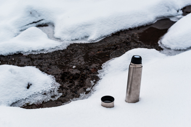 vacuum flask on snow near flowing mountain stream - Zdjęcie, obraz