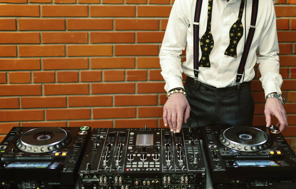 egy intelligens DJ keveri a zenét a konzolnál egy téglafalnak. - Fotó, kép
