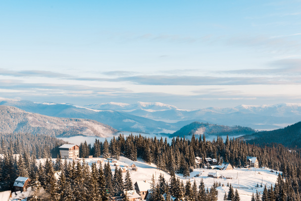 vista panorâmica da pequena aldeia em montanhas nevadas com pinheiros à luz do sol
 - Foto, Imagem