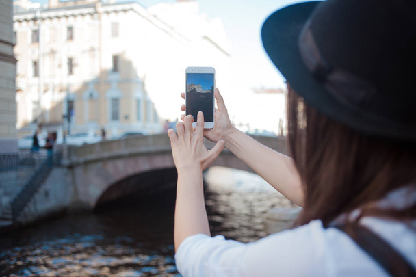 Turista in città scatta una foto su smartphone. Una giovane donna con un cappello nero e una camicia bianca
, - Foto, immagini