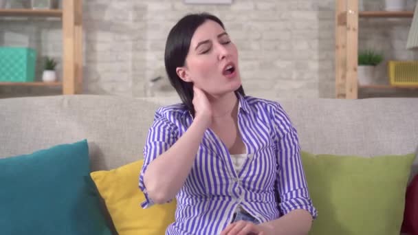 Young woman sitting on sofa and experiencing neck pain - Video