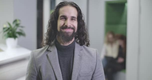Portrait of happy Middle Eastern man with long curly hair in formal business suit looking at camera and smiling. Handsome male office worker standing in open space. Cinema 4k ProRes HQ. - Imágenes, Vídeo