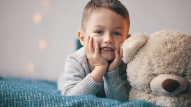 šťastný roztomilý malý chlapec mává rukou na kameru s medvídkem - Záběry, video