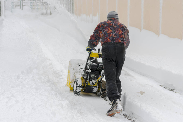 Ember működő hófúvó eltávolítja a havat a felhajtón. Az ember hófúvót használ. Ember takarítás hó járdán hófúvóval. - Fotó, kép