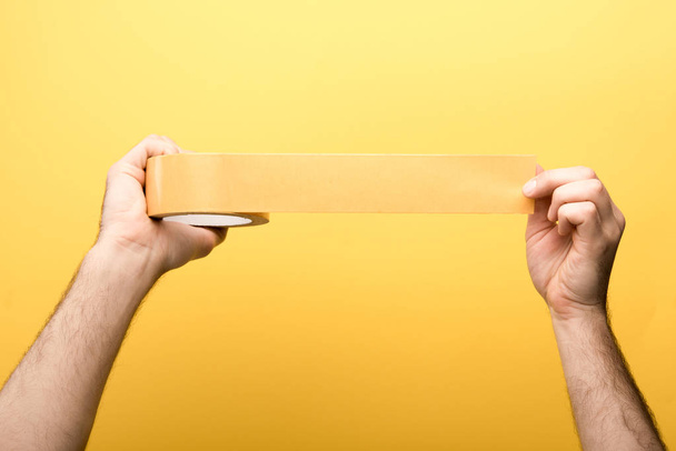 cropped view of man holding sticky tape on yellow background  - Foto, Imagen