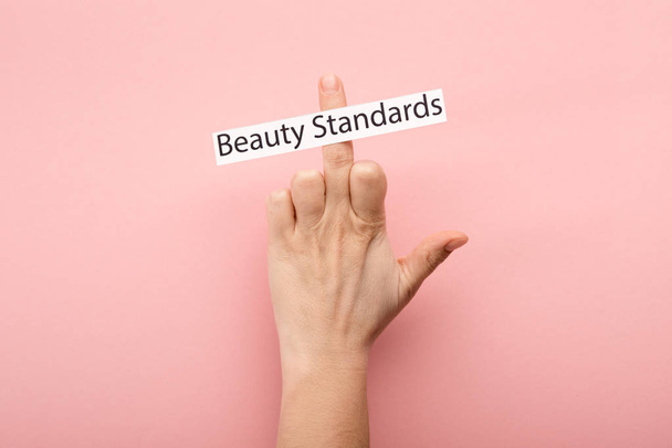 bijgesneden weergave van vrouw tonen middelvinger en kaart met schoonheid normen belettering op roze achtergrond  - Foto, afbeelding