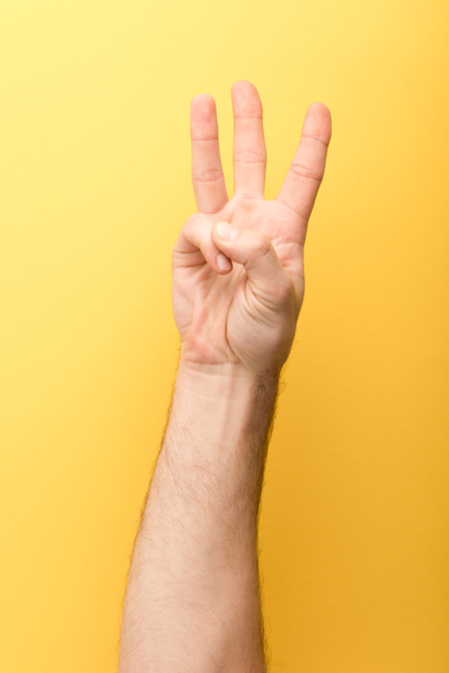 cropped view of man showing three fingers on yellow background  - Foto, Bild