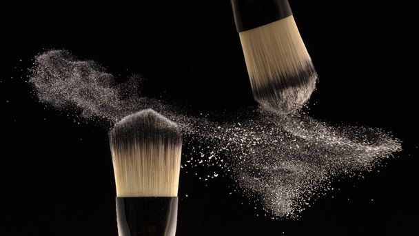 Concepto, maquillaje. Dos creadores de cepillos dispersan polvo sobre un fondo negro
. - Foto, Imagen