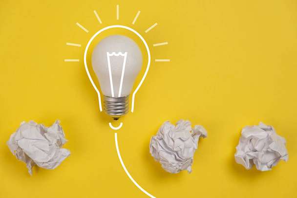 new idea concept with crumpled office paper and white light bulb on yellow background. Creative solution during brainstorming session concept. Flat lay, top view, copy space - Foto, imagen